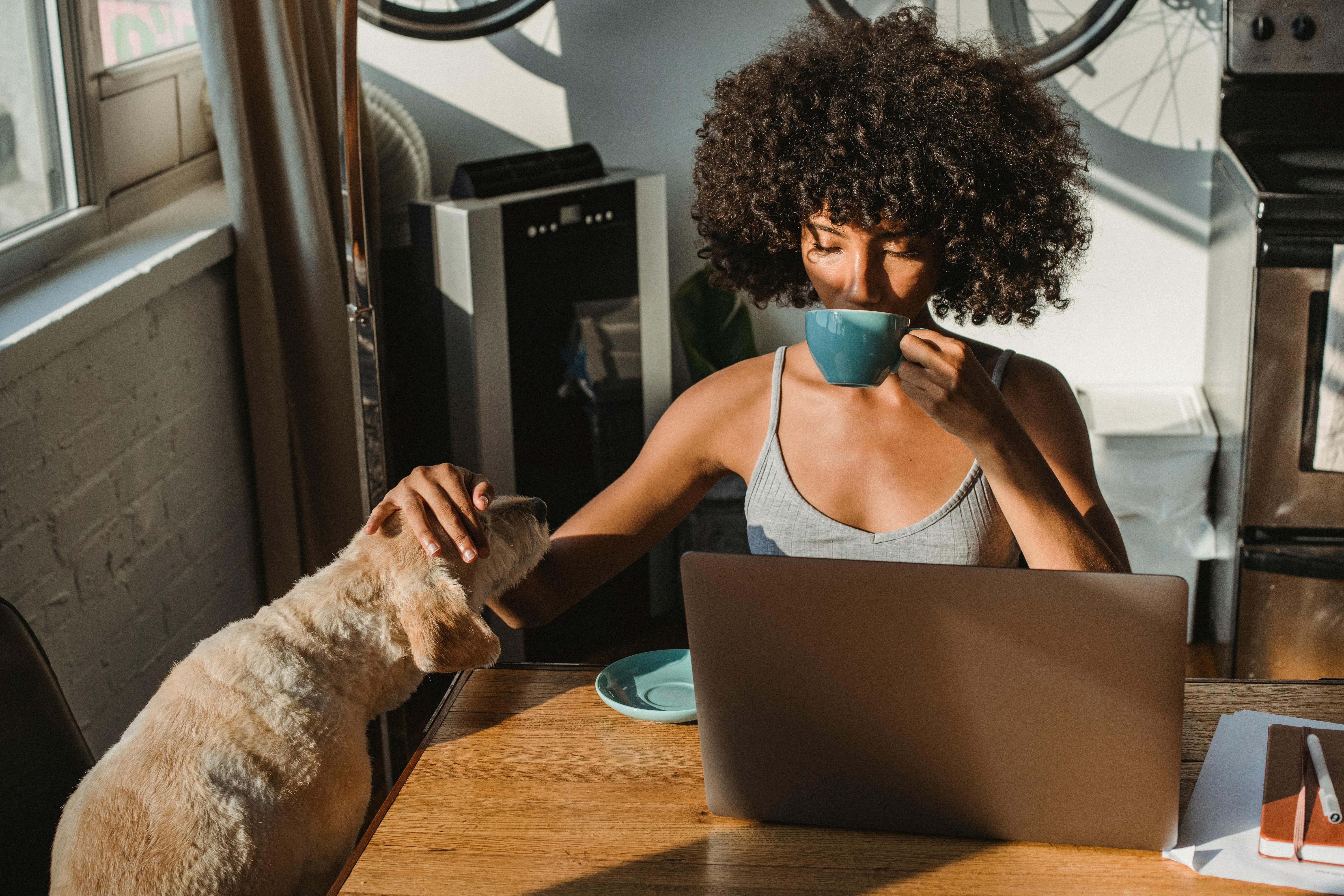 Person drinking from a cup while petting a dog